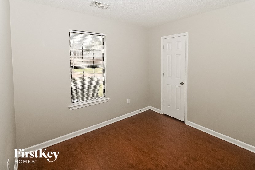 a bedroom with wood floors and a white door and a window