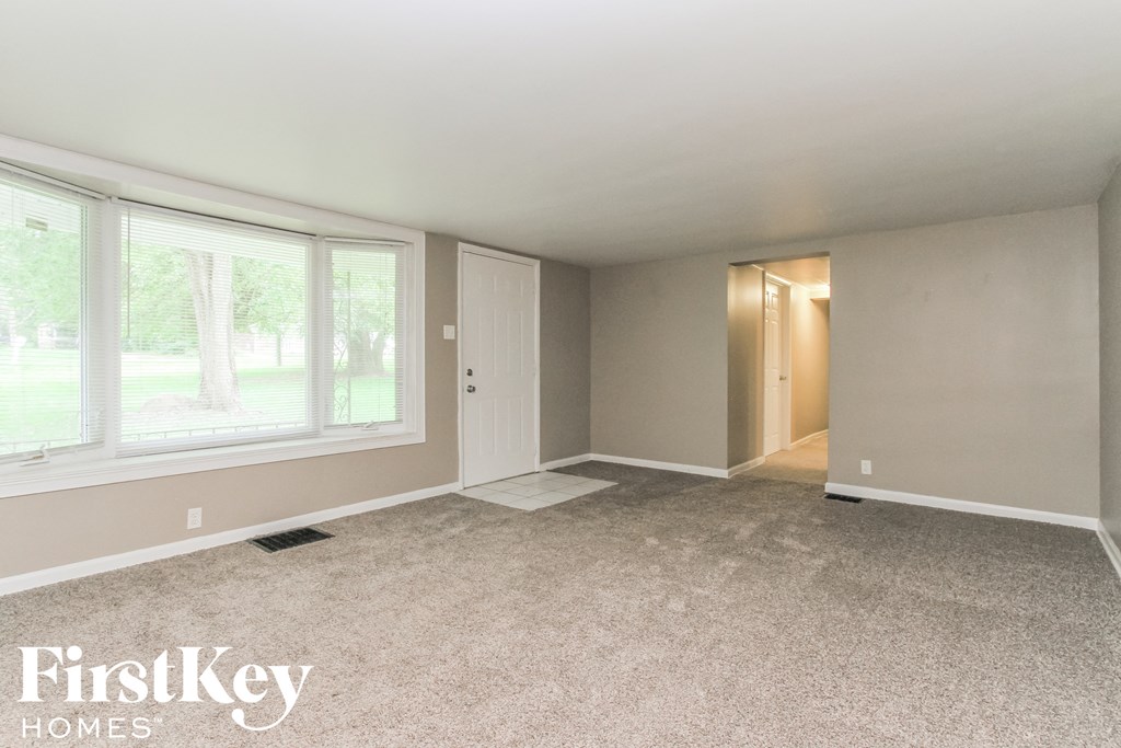an empty living room with large windows and carpeting
