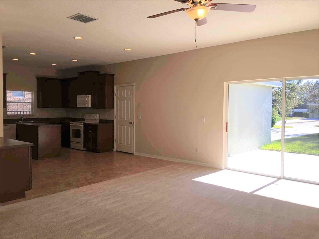 A sunny day in a spacious, empty room with a ceiling fan.