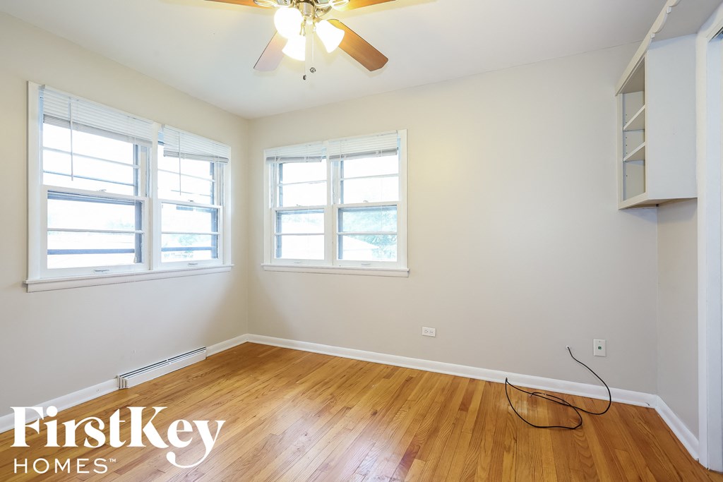 a bedroom with white walls and wood floors and a ceiling fan