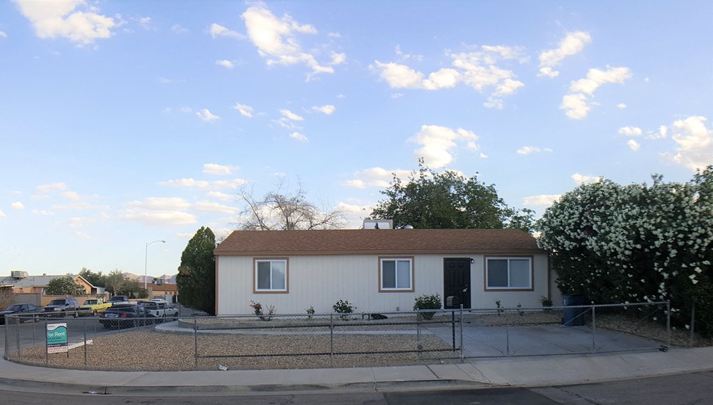 A small white house with a brown roof is surrounded by a fence.