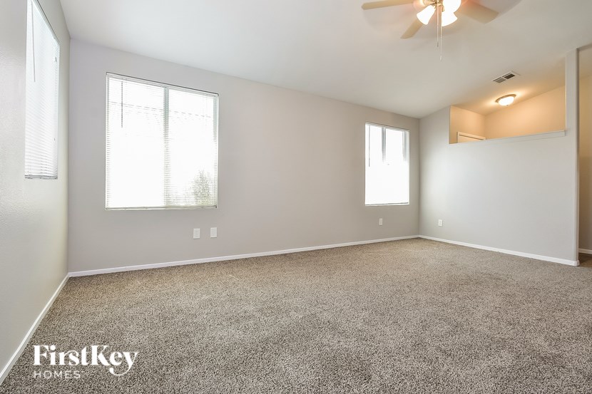 A spacious room with a carpeted floor, a ceiling fan, and two windows.