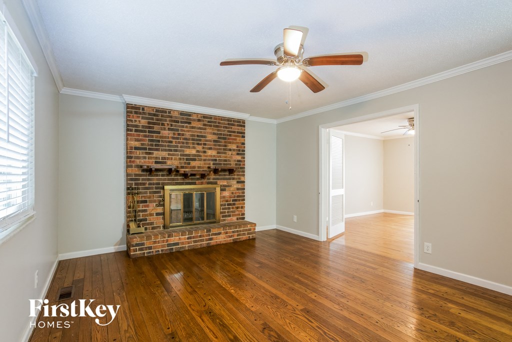 the living room of a house with a brick fireplace and a ceiling fan