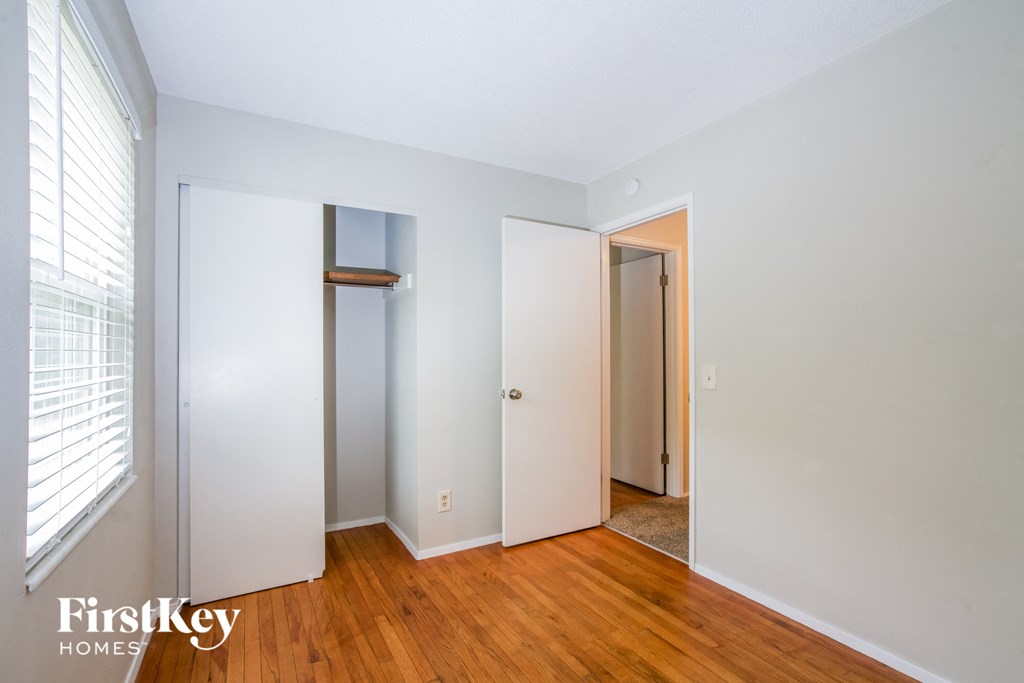 a bedroom with white walls and wood floors and a closet