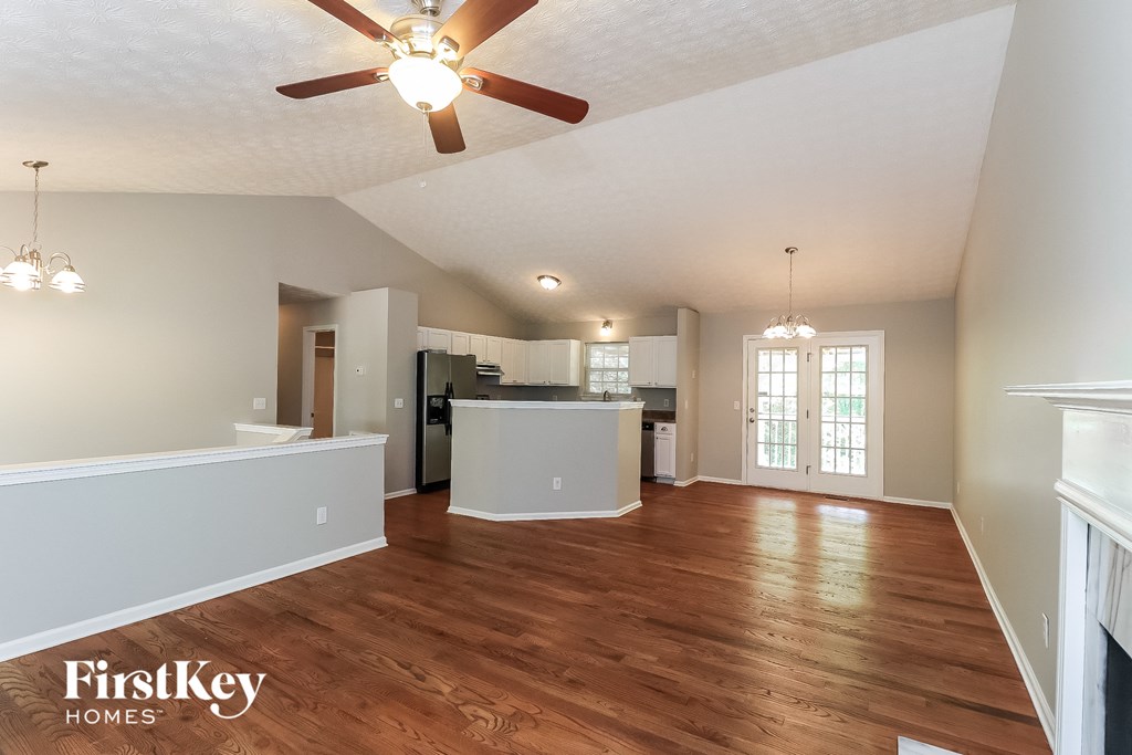 an empty living room with a ceiling fan and a kitchen