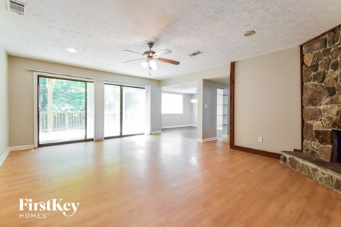 an empty living room with a stone fireplace and a ceiling fan