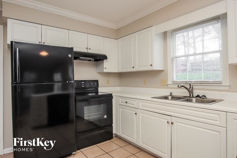 A black refrigerator with the words "FirstKey Homes" on it is in a kitchen with white cabinets.