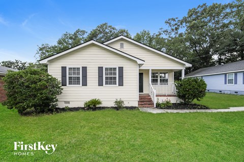 A small house with a porch and a tree in front.