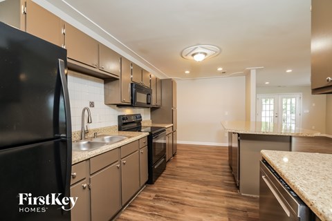 A kitchen with a black refrigerator and wooden floors.