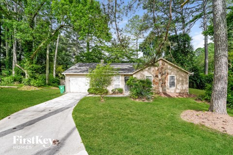 a small brick house with a driveway and a lawn and trees