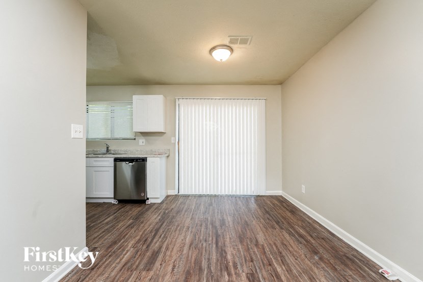 an empty living room with wood flooring and a kitchen