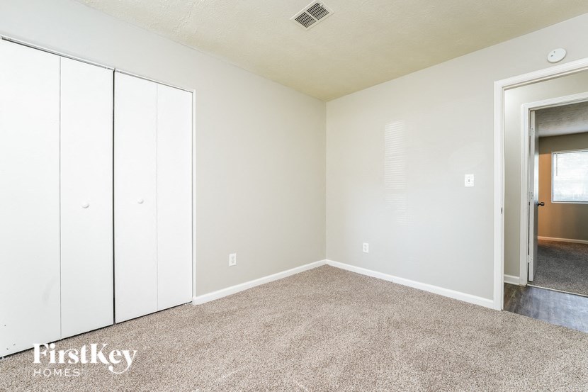 a bedroom with white cabinets and carpet and a door to a closet