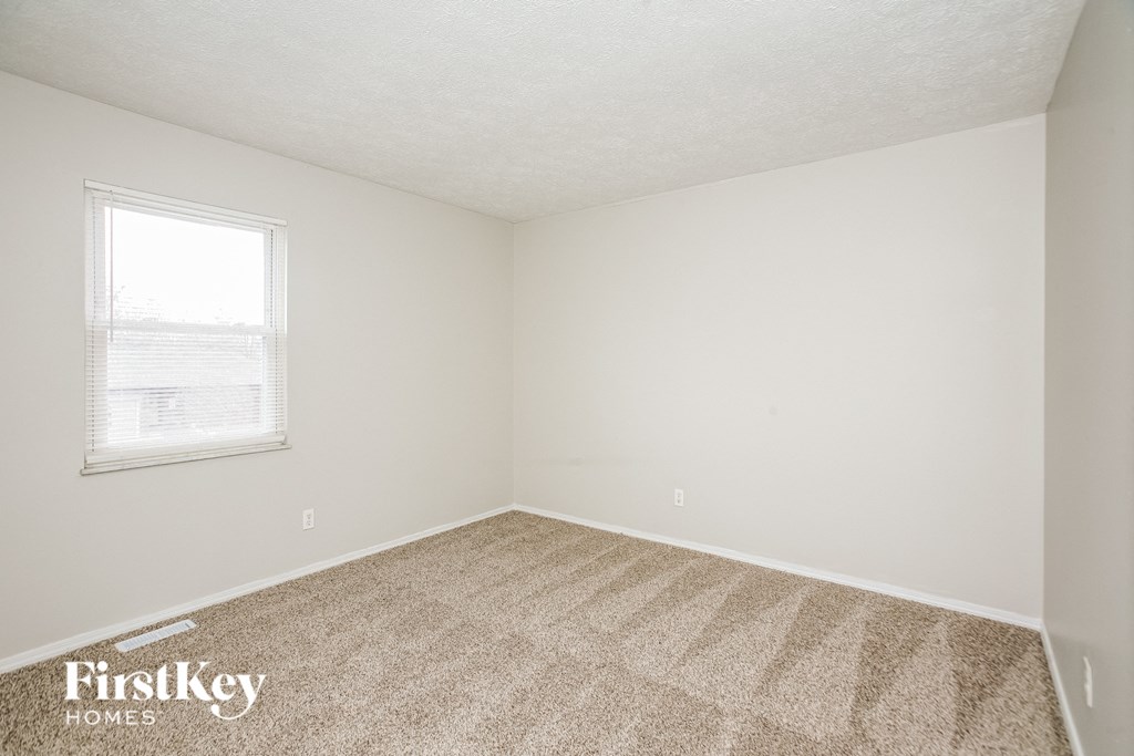 A room with a carpeted floor and a window with blinds.