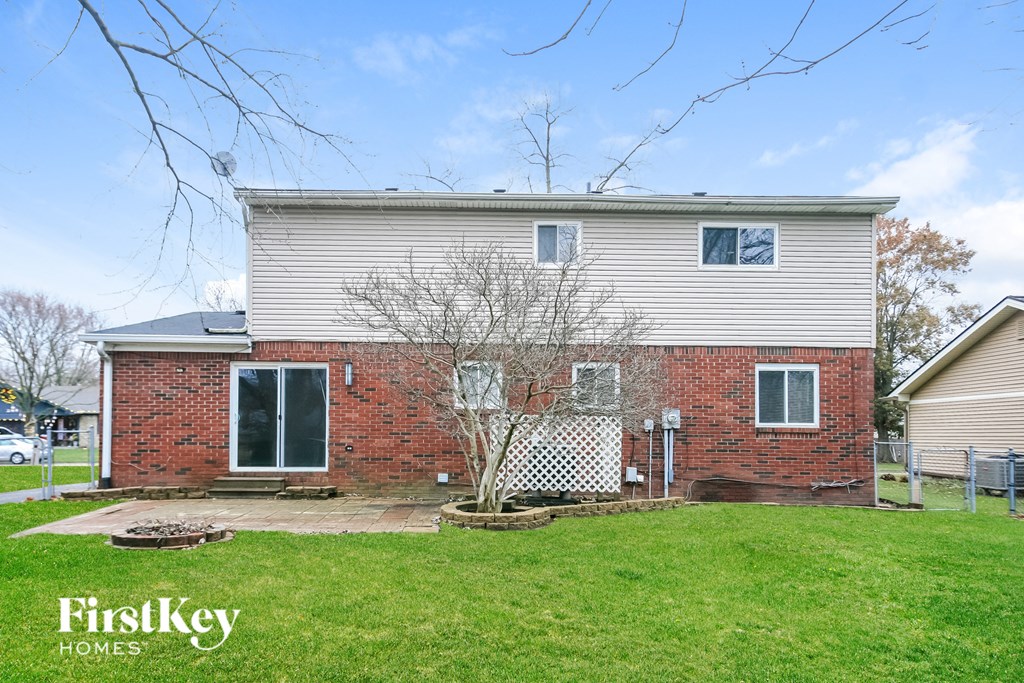 A brick house with a white siding extension and a tree in front.