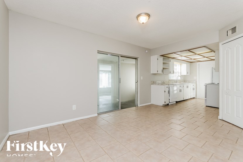 A spacious room with a tiled floor and a kitchen area in the background.