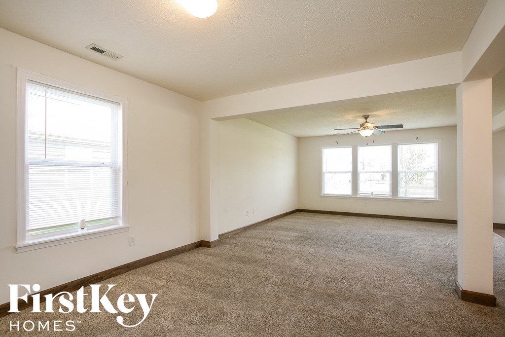 A spacious room with a carpeted floor and two windows.