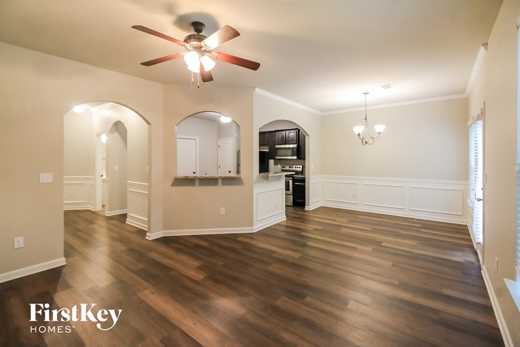 an empty living room with a ceiling fan and a kitchen