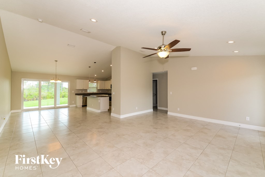 an empty living room with a ceiling fan and a kitchen