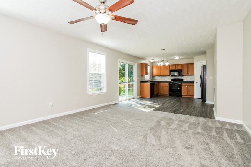 A spacious living room with a ceiling fan and a view of the kitchen.