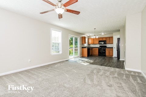 A spacious living room with a ceiling fan and a view of the kitchen.