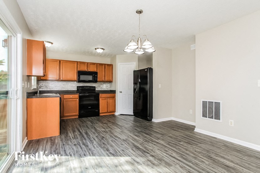 A kitchen with wooden floors and a black fridge.