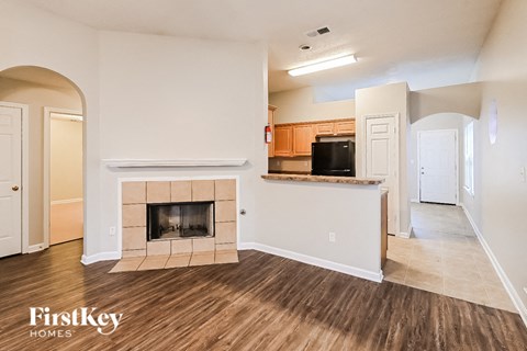 A living room with a fireplace and a kitchen in the background.