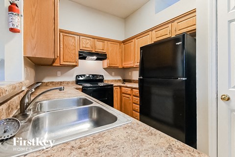 A kitchen with a black refrigerator, sink, and stove top oven.