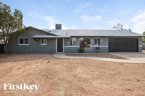A grey house with a black garage door and a tree in front of it.