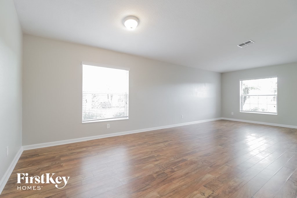 A spacious room with wooden flooring and two windows.