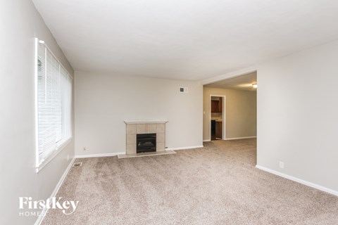 A spacious, empty room with a fireplace and a carpeted floor.