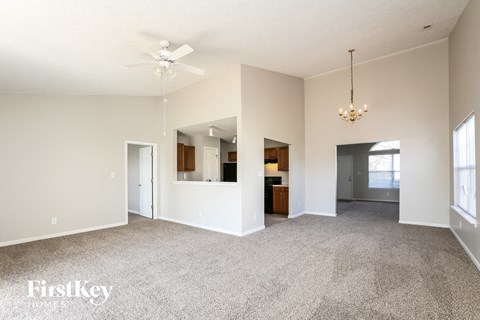 A spacious living room with a grey carpet and a chandelier hanging from the ceiling.