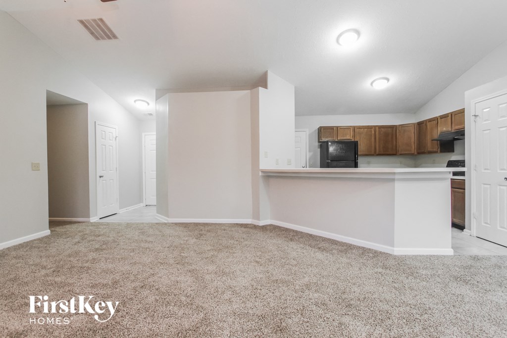 a living room with a kitchen and a carpeted floor
