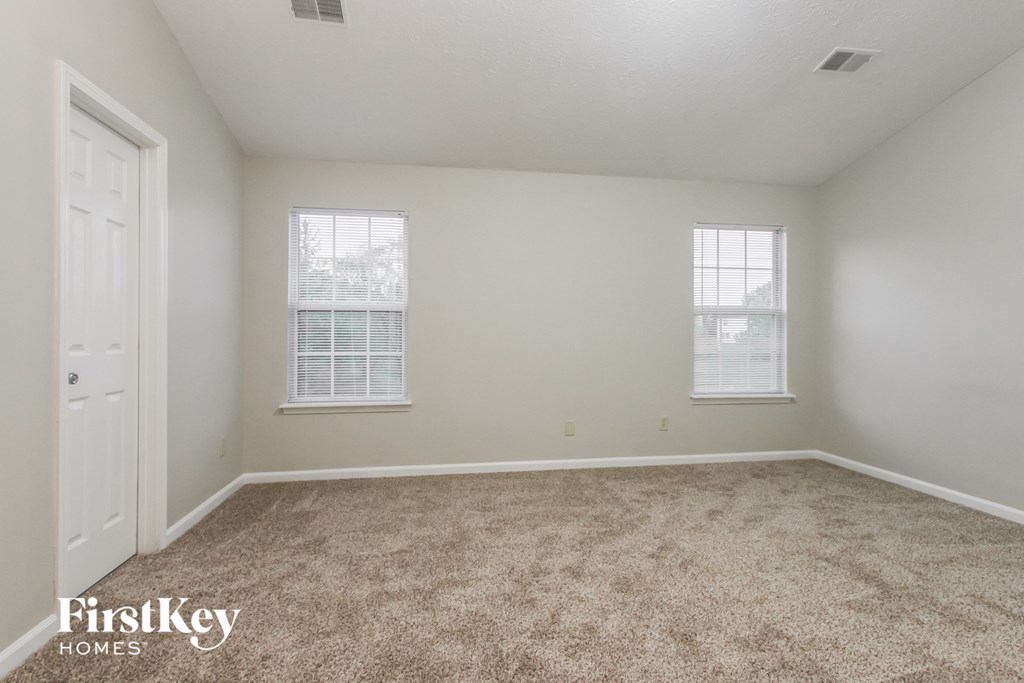 a spacious room with carpet and two windows