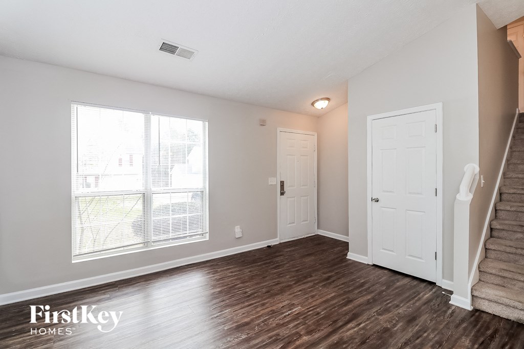 a living room with a staircase and a large window and a white door