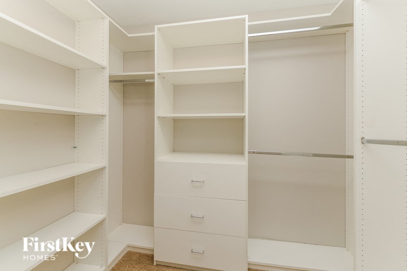a walk in closet with white shelves and drawers