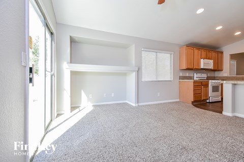 A spacious living room with a carpeted floor and a kitchen area with wooden cabinets and a white stove.