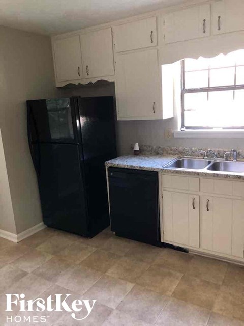 A black refrigerator and black dishwasher in a kitchen with white cabinets.