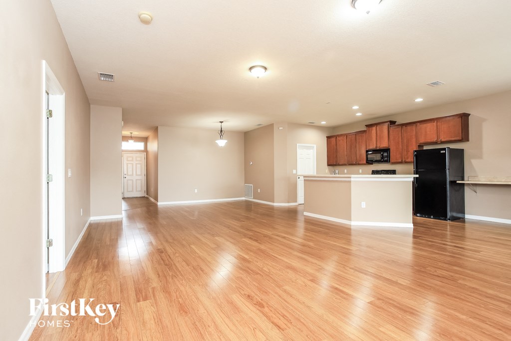 A spacious living room with wooden floors and a kitchen area in the background.