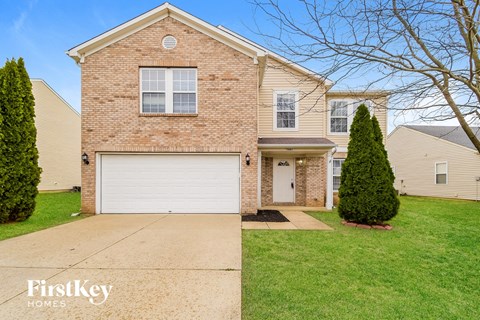 A brick house with a garage door and a tree in front.