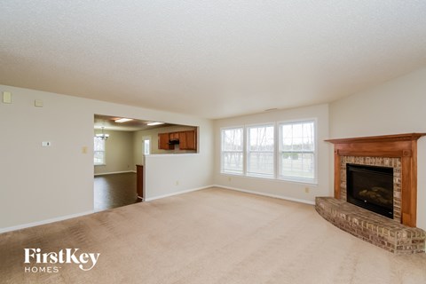 A spacious living room with a fireplace and a view of a hallway and kitchen.