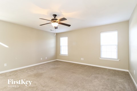 A spacious room with a ceiling fan and two windows.