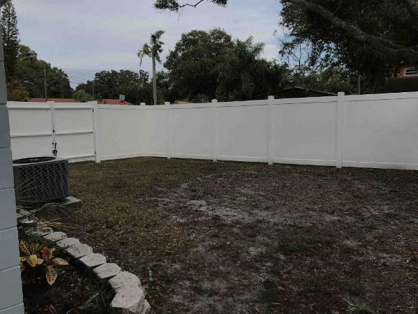 A white fence encloses a yard with a grassy area and a small garden bed.