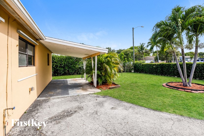 a small yellow house with a driveway and a lawn with palm trees
