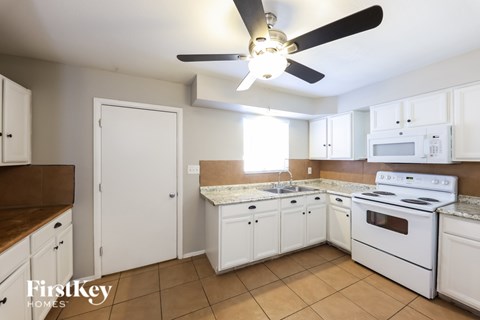 A kitchen with white cabinets and appliances, a ceiling fan, and a tile floor.