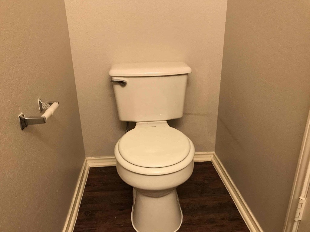 A white toilet in a small bathroom with wood flooring.