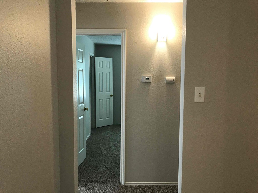A hallway with a light on the wall and a door at the end.