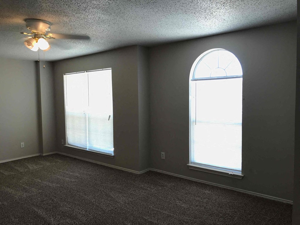 A room with a ceiling fan and two windows.
