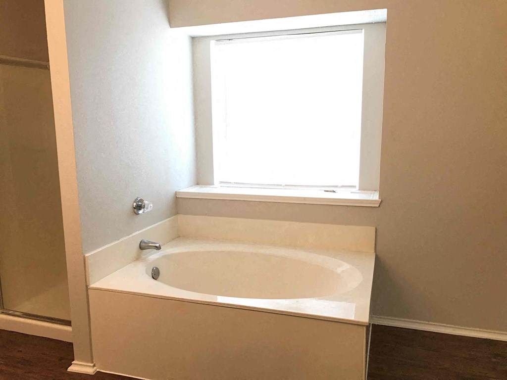 A white bathtub with a window above it in a bathroom.