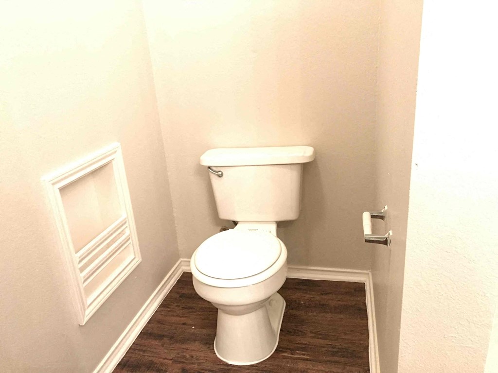 A white toilet in a small bathroom with wood flooring.