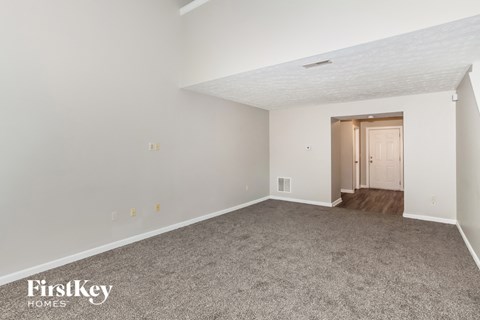 A spacious empty room with a carpeted floor and a door on the right side.